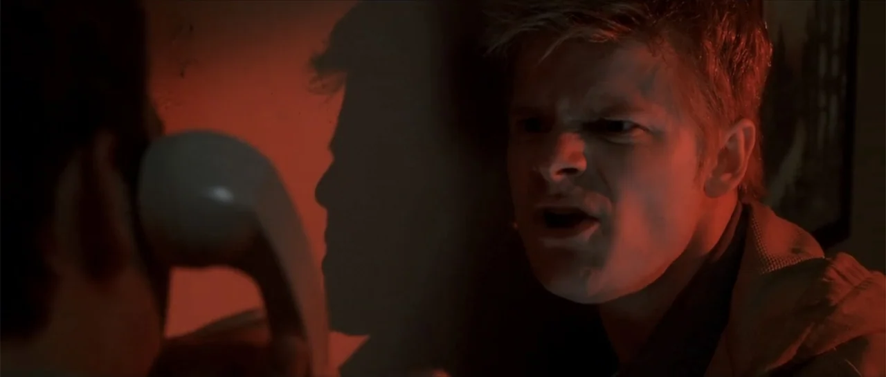 Joy Ride (2001) movie still: closeup — A dark indoor setting features a man standing against a wall lit by red light. He yells while looking at…