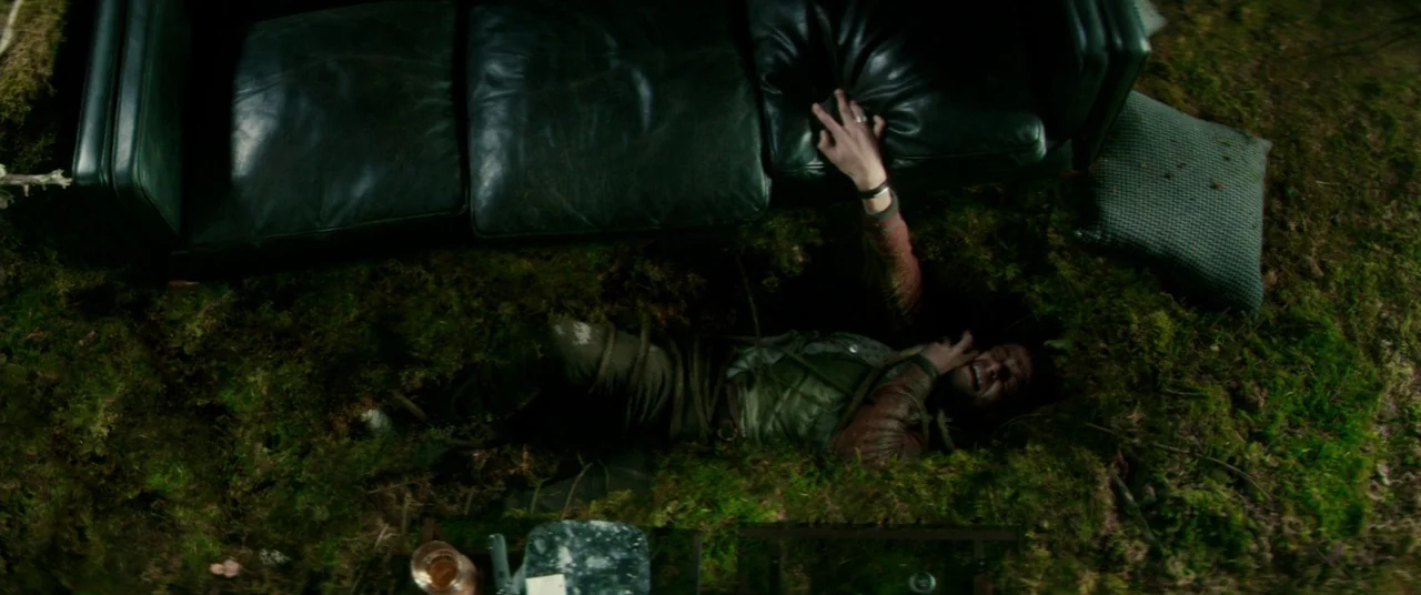 Horns (2013) movie still: wide — A man lies inside a shallow earthen pit covered in thick green mossy vegetation. He stretches one hand upward to…