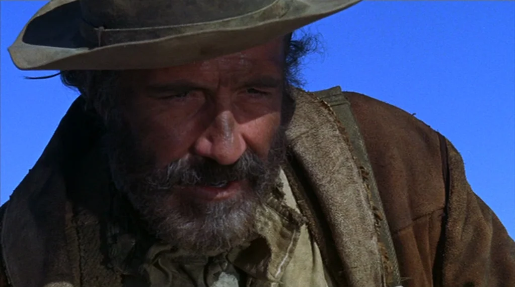 The Ballad of Cable Hogue (1970) movie still: closeup — An arid, sun-drenched outdoor environment with a clear, cloudless sky behind the subject. A…
