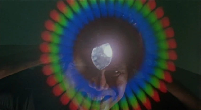 Boxer’s Omen (Mo) (1983) movie still: closeup — A man is positioned closely to the camera lens in a dark, interior space. A bright light source…