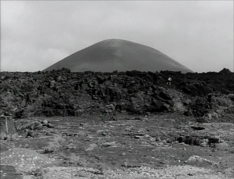 Even Dwarfs Started Small (1970) movie still: wide — A desolate volcanic landscape features jagged dark lava rocks under a light overcast sky. A…