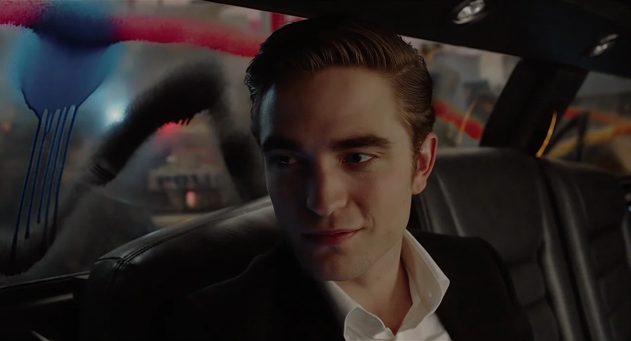 Cosmopolis (2012) movie still: closeup — The interior of a limousine at night with graffiti visible on the window glass. A young man sits in the…