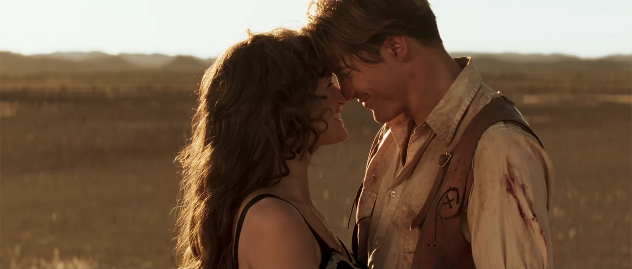 The Mummy (1999) movie still: medium — A vast, open desert landscape stretches toward the horizon during the golden hour. A man and a woman stand…