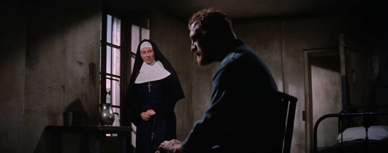 Lust For Life (1956) movie still: medium — A sparsely furnished room with stone walls and a small barred window. A woman dressed as a nun stands…