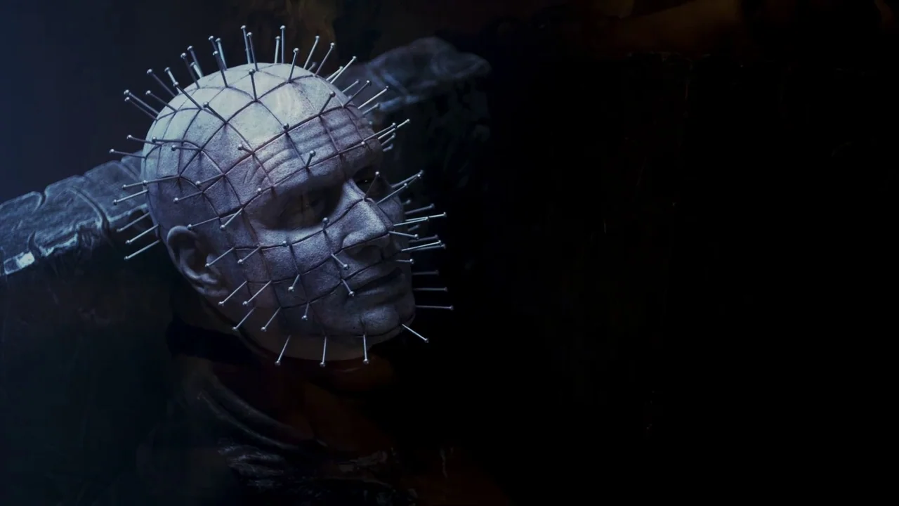 Hellraiser: Judgement (2018) movie still: closeup — A pale, bald humanoid figure with metal pins in their skin occupies a dark space. The figure…