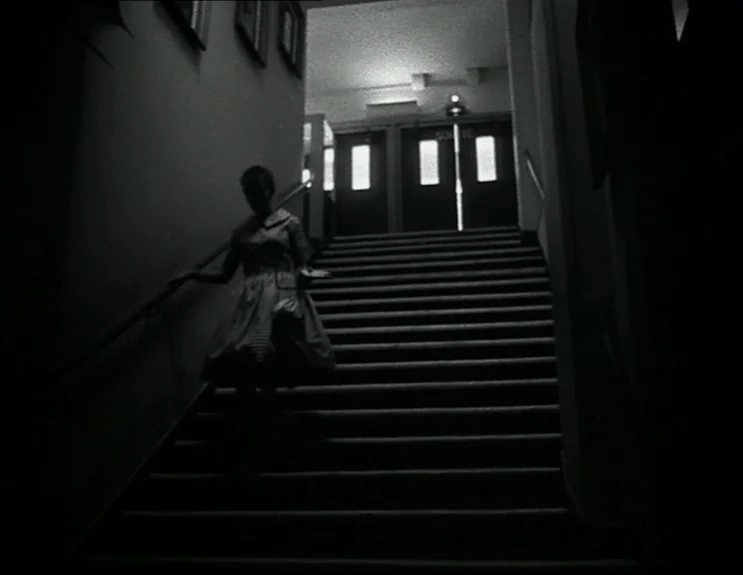 À Bout De Souffle (Breathless) (1960) movie still: fullbody — A dark, dimly lit indoor staircase features a landing with two exit doors. A woman in…