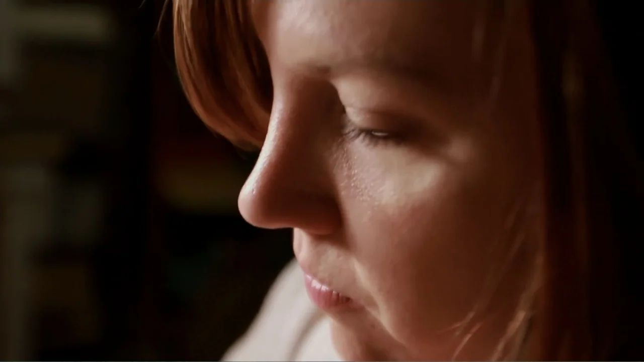 The (Dead Mothers) Club (2014) movie still: closeup — An interior space provides a dark, out-of-focus background for the subject's face. The woman…