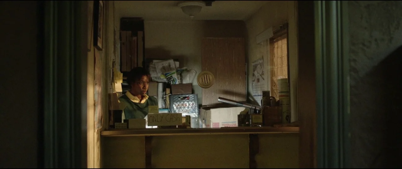 Lowlife (2017) movie still: medium — A cluttered administrative workstation features a service window and several stacked boxes.