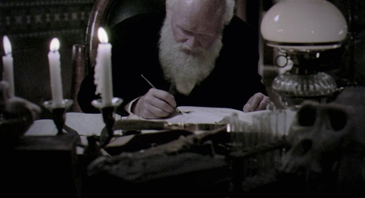 Adaptation (2002) movie still: medium — A dimly lit room contains a desk cluttered with scientific apparatus and papers. An elderly man sits at the…