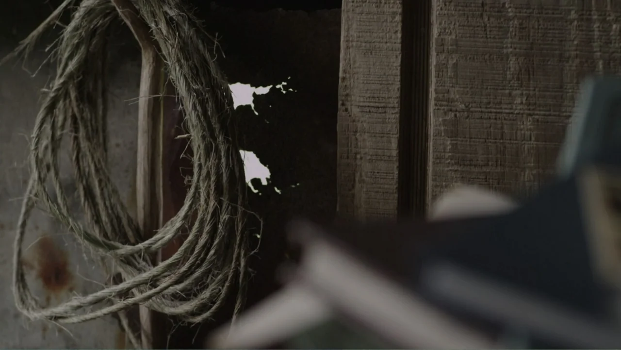 Boy (2010) movie still: closeup — A rustic wooden structure features a coil of coarse rope hanging on the wall. A jagged opening in the timber…