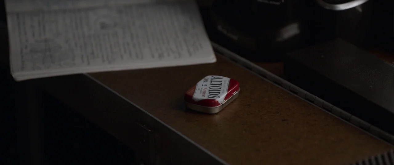 Ant-Man and the Wasp (2018) movie still: closeup — A small red and white metal mint tin sits on a dark brown desk. A notebook with handwritten notes…