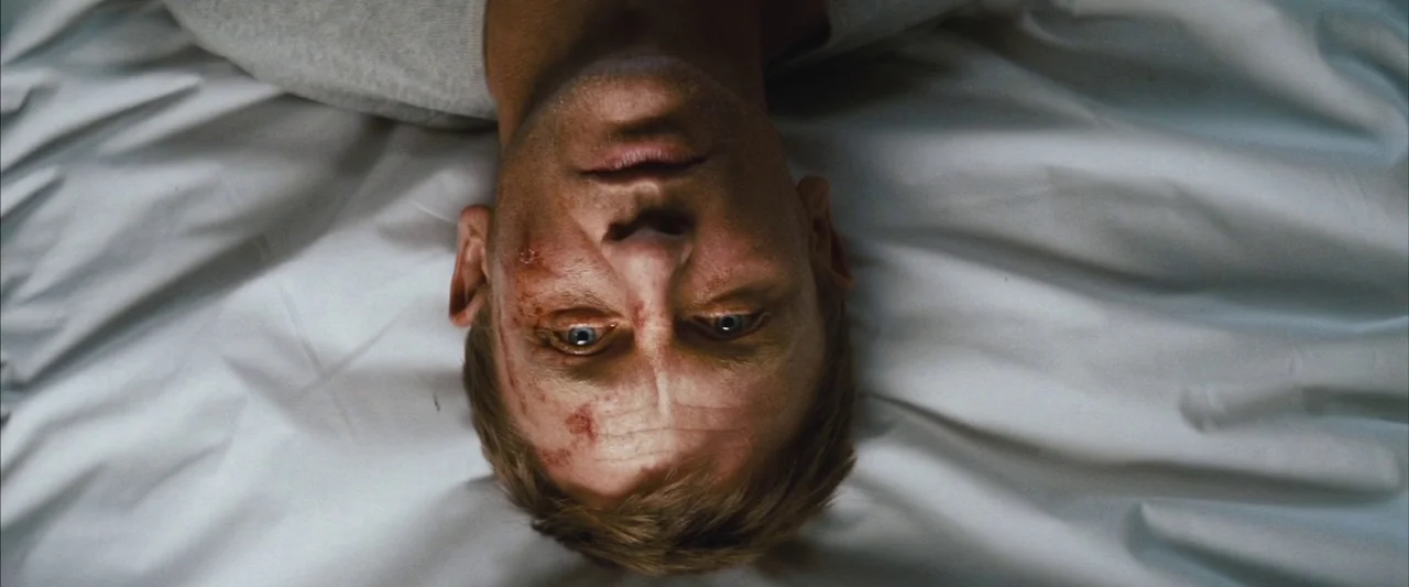 Layer Cake (2004) movie still: closeup — A man lies on a plain white surface that fills the frame. The subject faces the camera directly while lying…