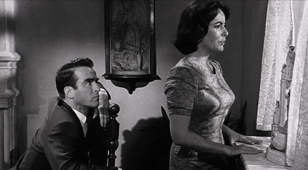 Suddenly, Last Summer (1959) movie still: medium — A dark indoor space featuring a man in a suit and a standing woman. The woman stands by a window…