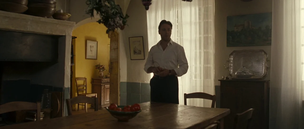 A Good Year (2006) movie still: medium — A rustic dining room features a long wooden table and a yellow-walled adjacent room. A man stands near a…