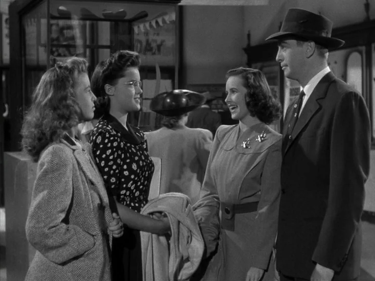 Shadow of a Doubt (1943) movie still: medium — A public interior space with glass-cased signage and a bustling station atmosphere. A group of four…