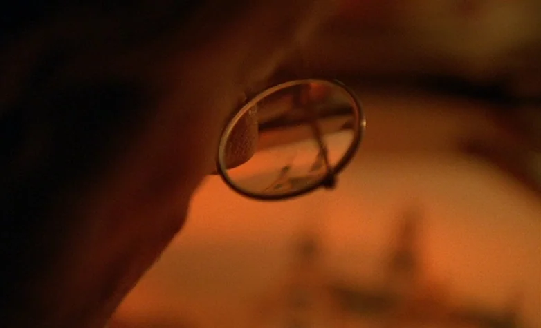 The Double Life of Véronique (1991) movie still: closeup — A close-up view shows a metal jeweler's loupe held against a dark, blurred background.…