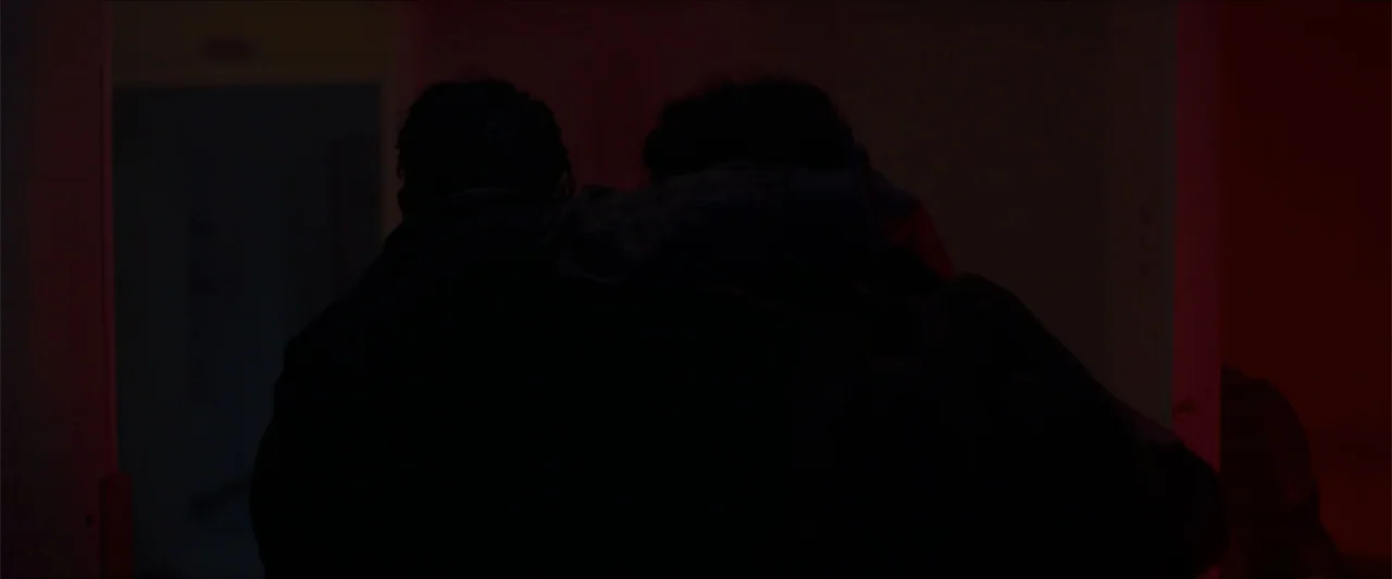 Apocalypse Z: The Beginning of the End (2024) movie still: medium — A dimly lit indoor corridor with red light hitting the walls from one side. Two…