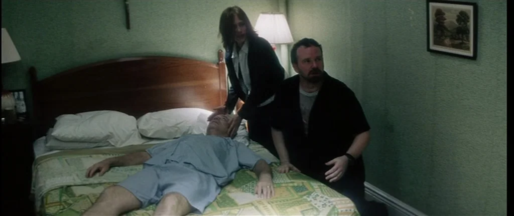 Bringing Out The Dead (1999) movie still: medium — A green-walled room contains a double bed with a patterned quilt and two lamps. A woman and a man…