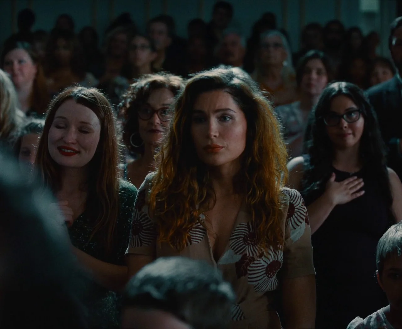 Monica (2022) movie still: medium — A crowded hall filled with people attending a formal gathering. The central woman stands looking forward while…