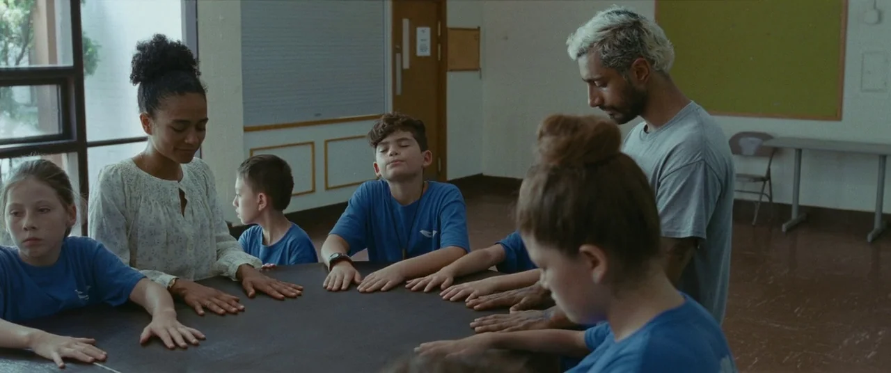 Sound of Metal (2019) movie still: medium — A group of children and two adults sit together at a circular table. They have their hands resting on…