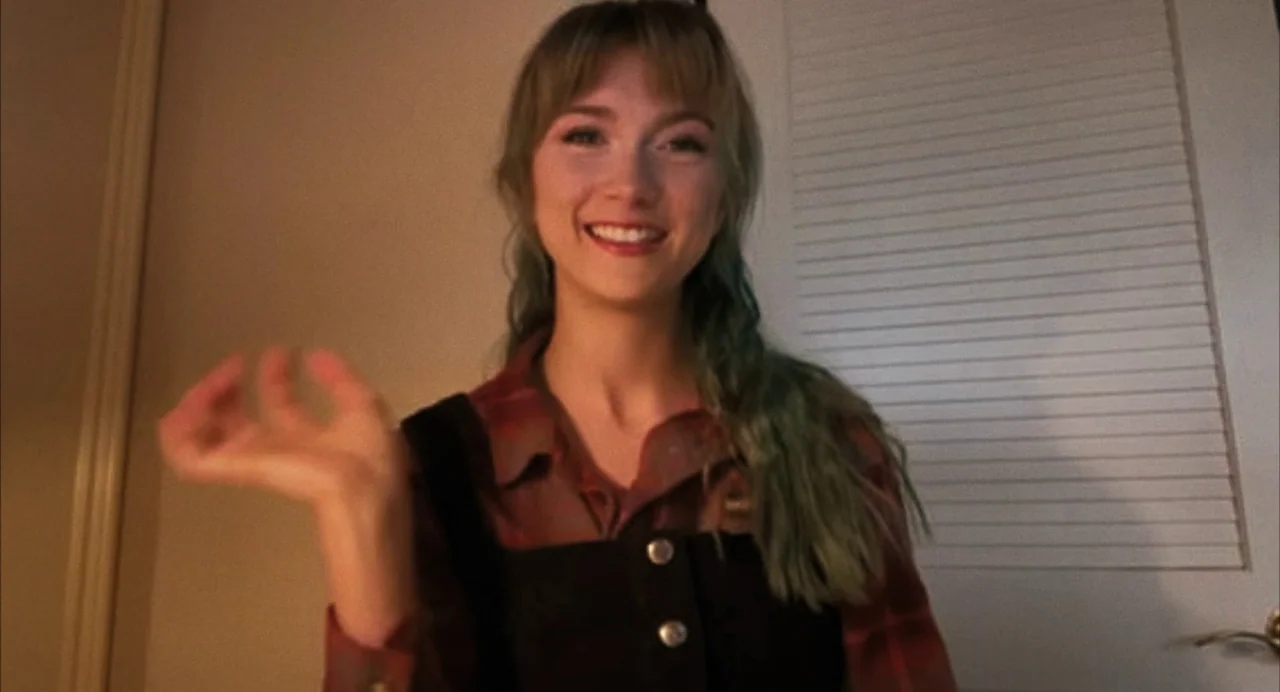 When You Finish Saving The World (2022) movie still: medium — A room with a closed white louvered door in the background. A young woman waves her…