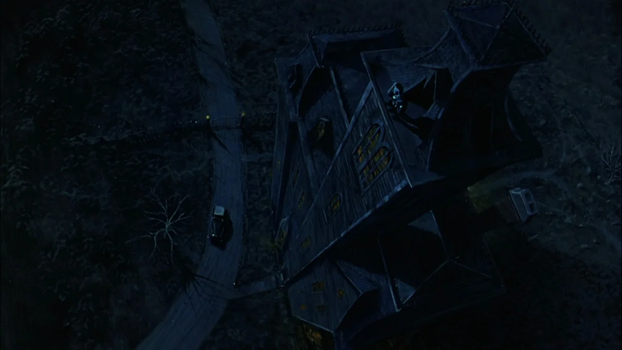 Addams Family Values (1993) movie still: establishing — A dark gothic mansion sits at night next to a winding dirt road. A small vintage car travels…