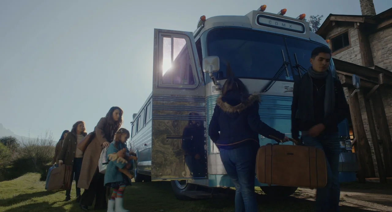 Dating Santa (2023) movie still: wide — A group of people board a vintage passenger bus at a grassy outdoor area. They carry luggage and personal…