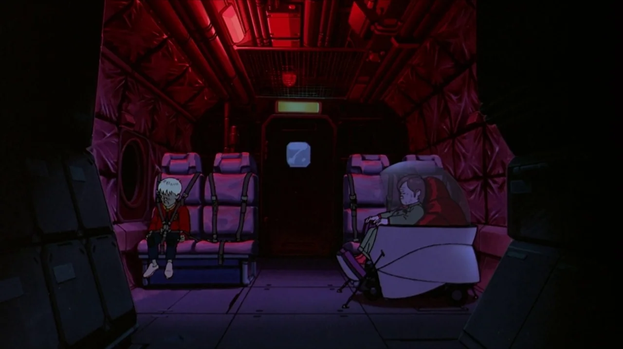 Akira (1988) movie still: wide — A confined aircraft cabin features dark red walls and an overhead emergency lighting system. Two passengers occupy…
