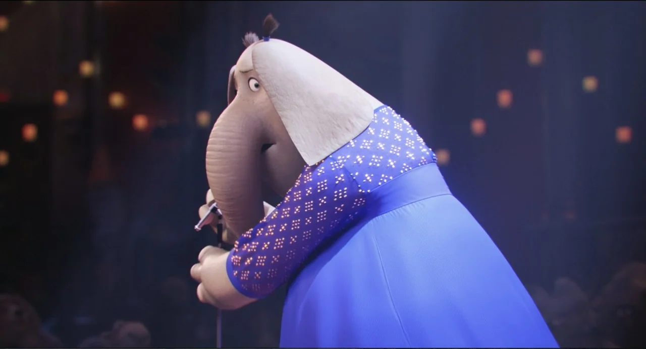 Sing (2016) movie still: medium — A dark performance stage with blurred lights in the deep background. An elephant character in a blue dress stands…