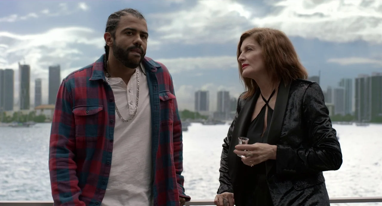 Velvet Buzzsaw (2019) movie still: medium — A man and woman stand on the deck of a boat with a city skyline visible across the water. The sky is…