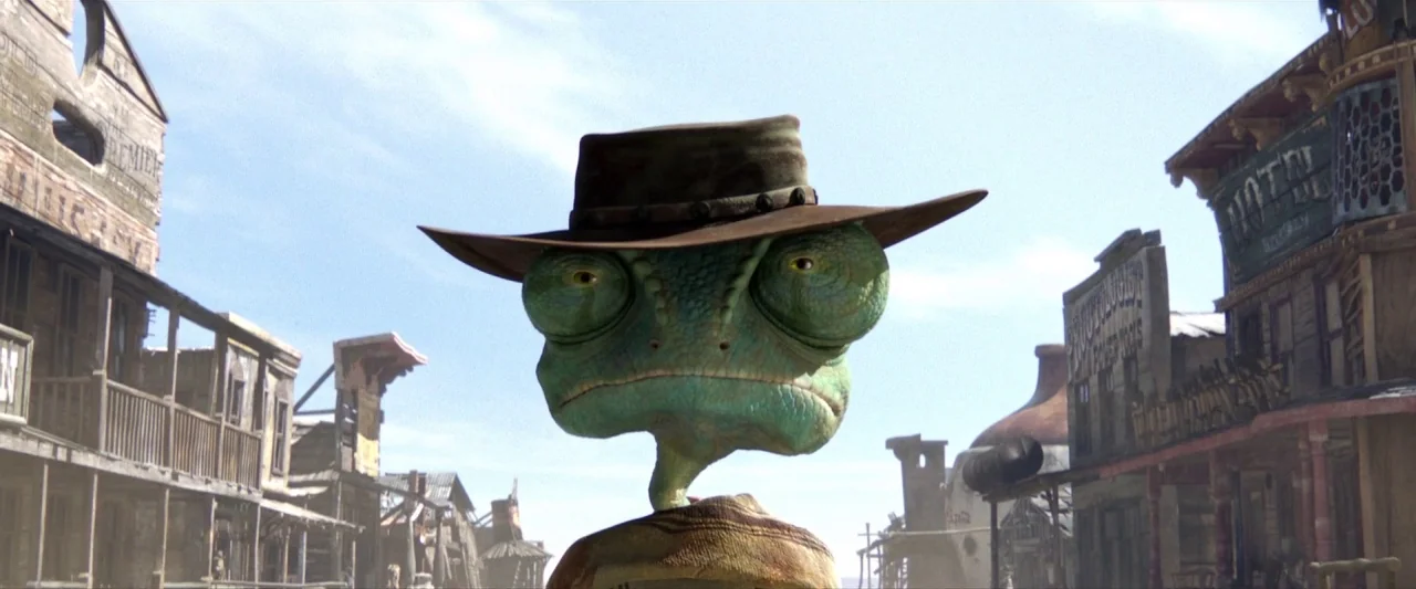 Rango (2011) movie still: closeup — A dusty main street in a desolate western town lined with wooden storefronts. A green chameleon character…