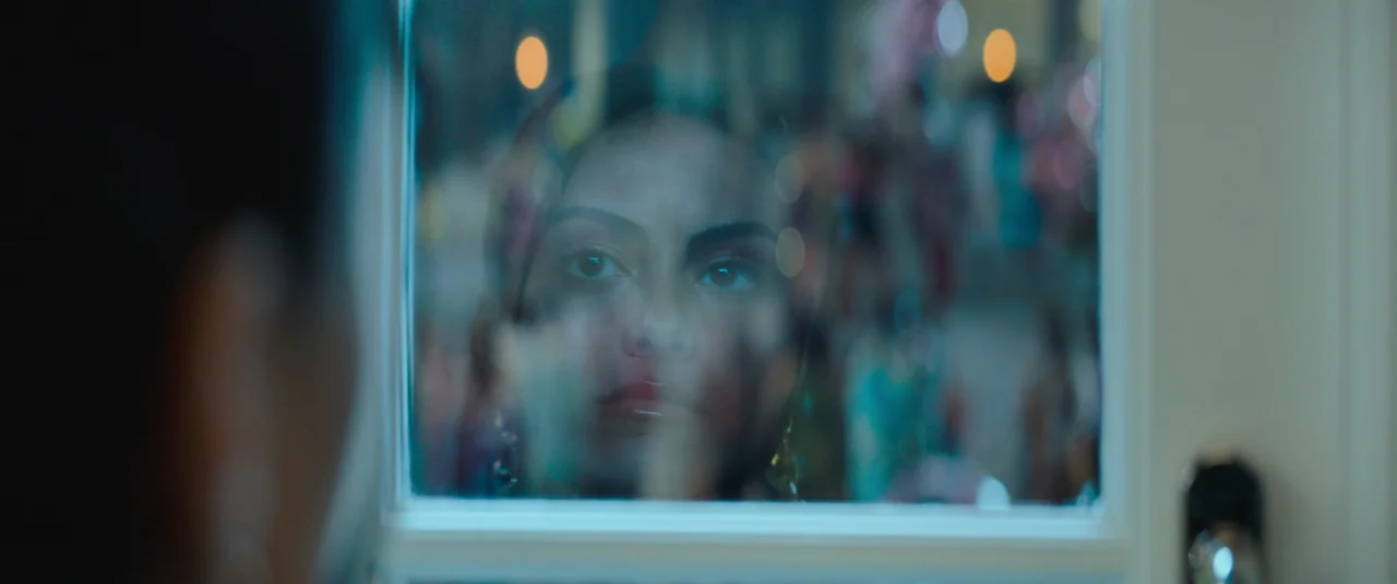 Do Revenge (2022) movie still: closeup — A woman's face appears as a reflection in a windowpane at night. Blurred lights are visible in the…