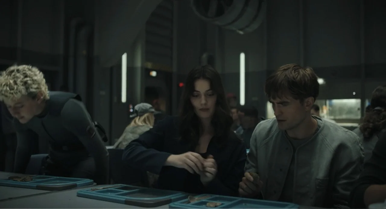 Mickey 17 (2025) movie still: medium — A utilitarian industrial space with metallic walls and minimalist furniture features several people dining.…