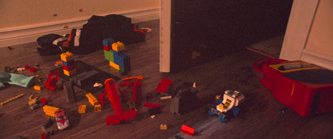 Skinamarink (2022) movie still: wide — A cluttered floor is strewn with colorful plastic building blocks and a red toy. The scene is empty with no…
