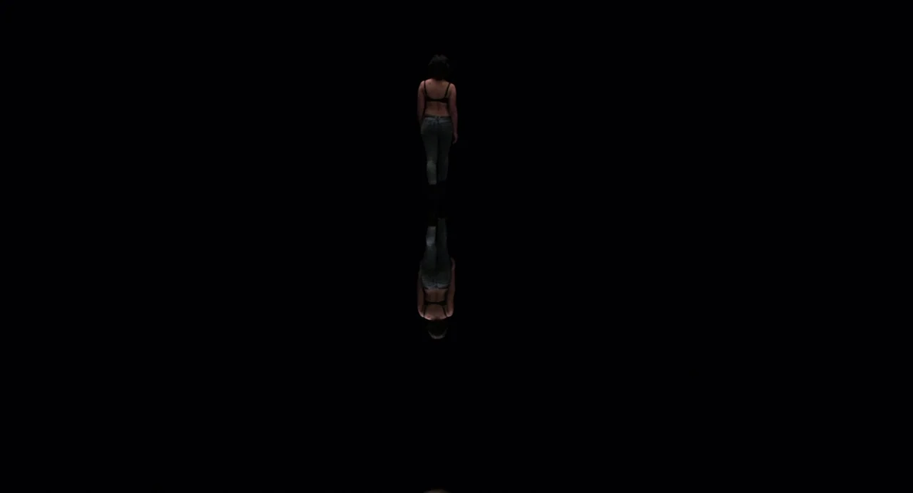 Under The Skin (2013) movie still: wide — A figure walks across a perfectly reflective, pitch-black surface in a featureless environment. The…