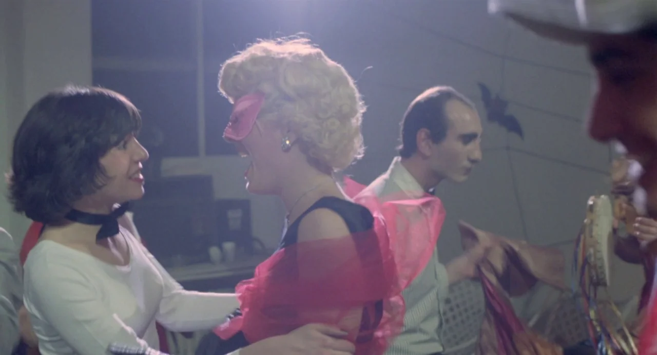 Ms. 45 (1981) movie still: medium — A group of people gather at a 1980s party with simple wall decorations. Two young women face each other while…