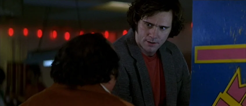 Man On The Moon (1999) movie still: medium — A dimly lit arcade interior features rows of red neon lights on the back wall. A man in a blazer looks…