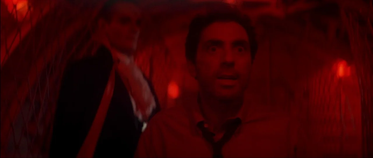 The Monster Squad (1987) movie still: medium — A dark hallway illuminated by an intense red light source. A man stares forward in distress while a…