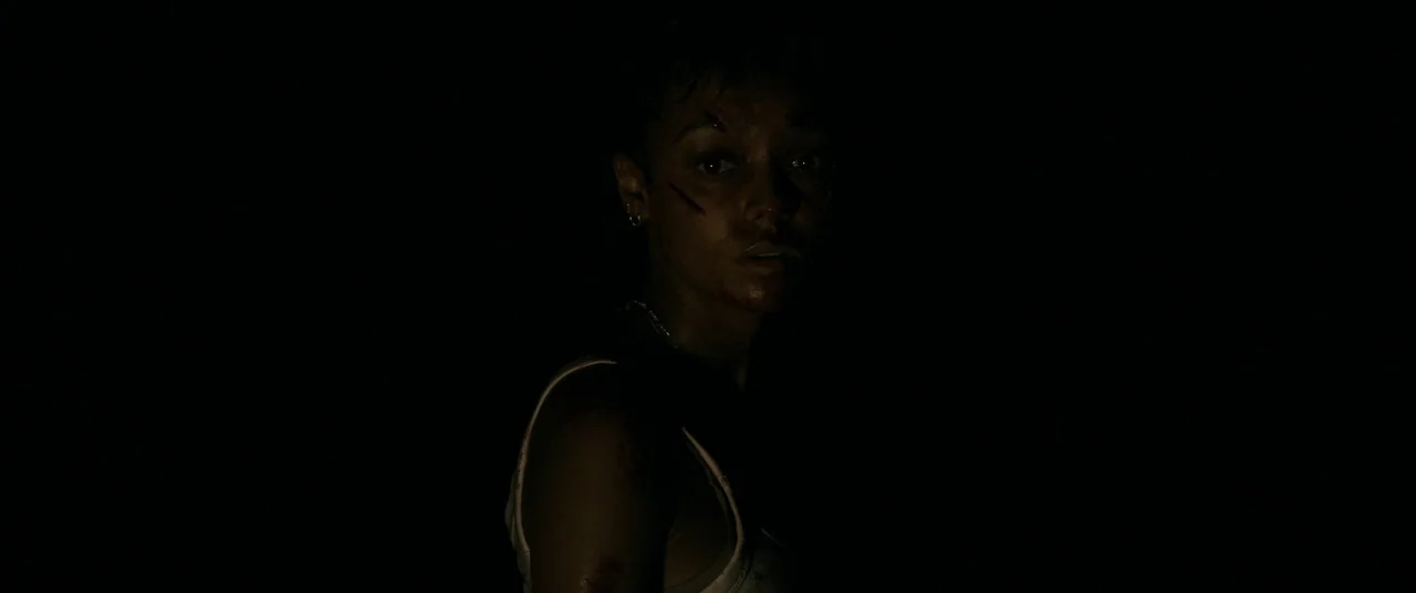 Talk To Me (2022) movie still: closeup — A dark, undifferentiated environment obscures all details of the surrounding physical space. A young woman…