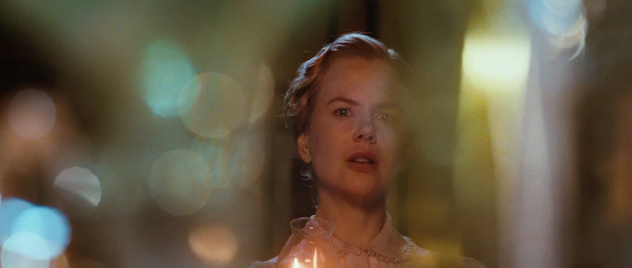 Australia (2008) movie still: closeup — A woman stands in a dim, dark interior space holding a small glowing lantern. She faces forward with a…