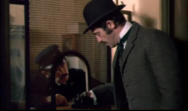 The Thief of Paris (1967) movie still: medium — An interior ticket booth with wire mesh separating the clerk from a customer. A man in a suit…