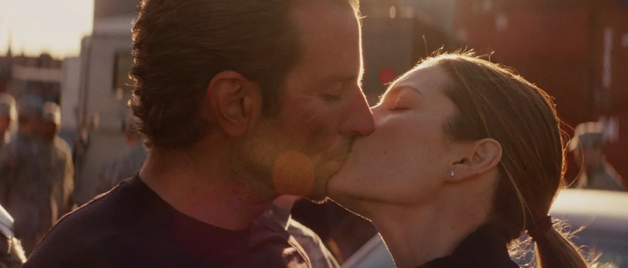 The A-Team (2010) movie still: closeup — A man and woman share a kiss in an industrial setting at sunset. The couple stands facing each other in…
