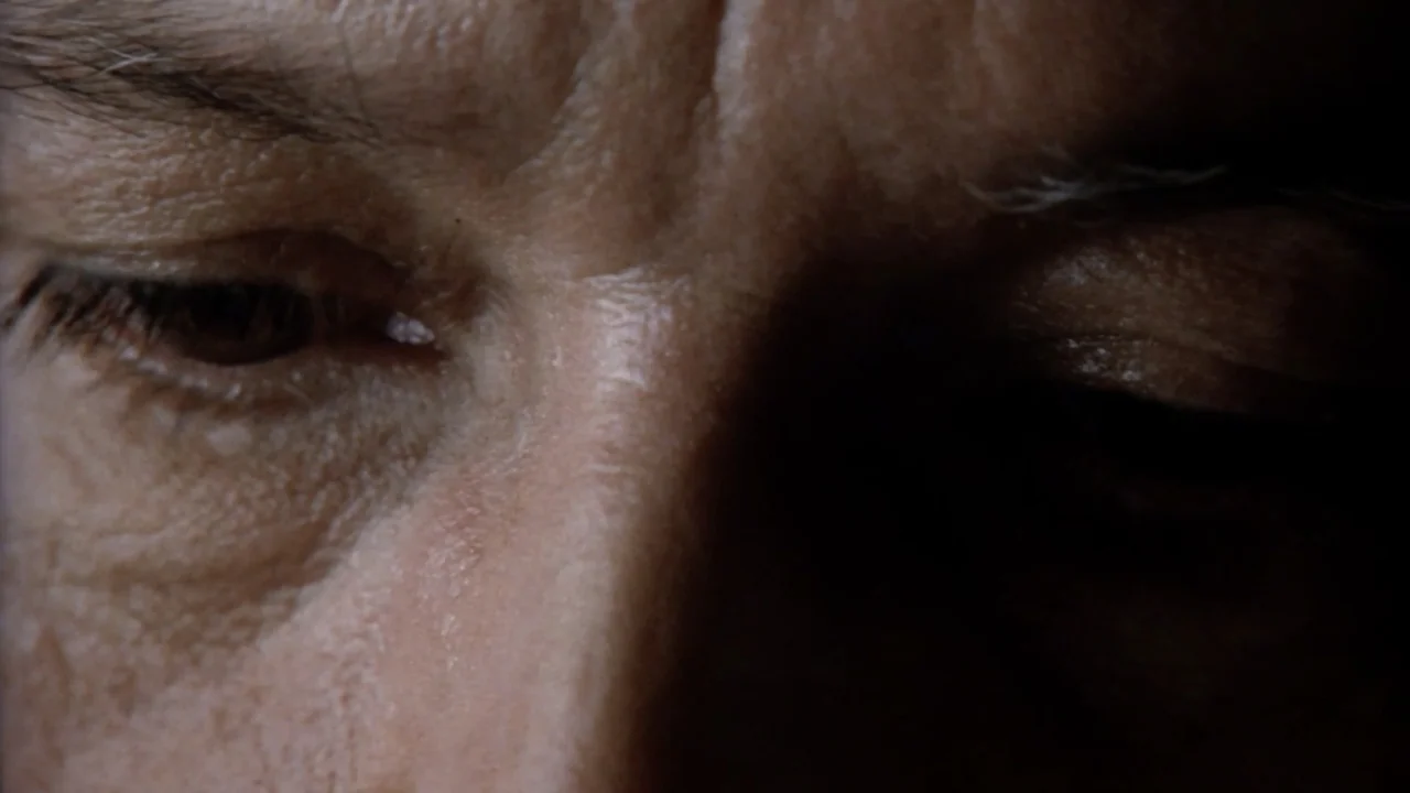 Suspect Zero (2004) movie still: closeup — An interior space is kept in near darkness with minimal environmental detail. A man with visible facial…