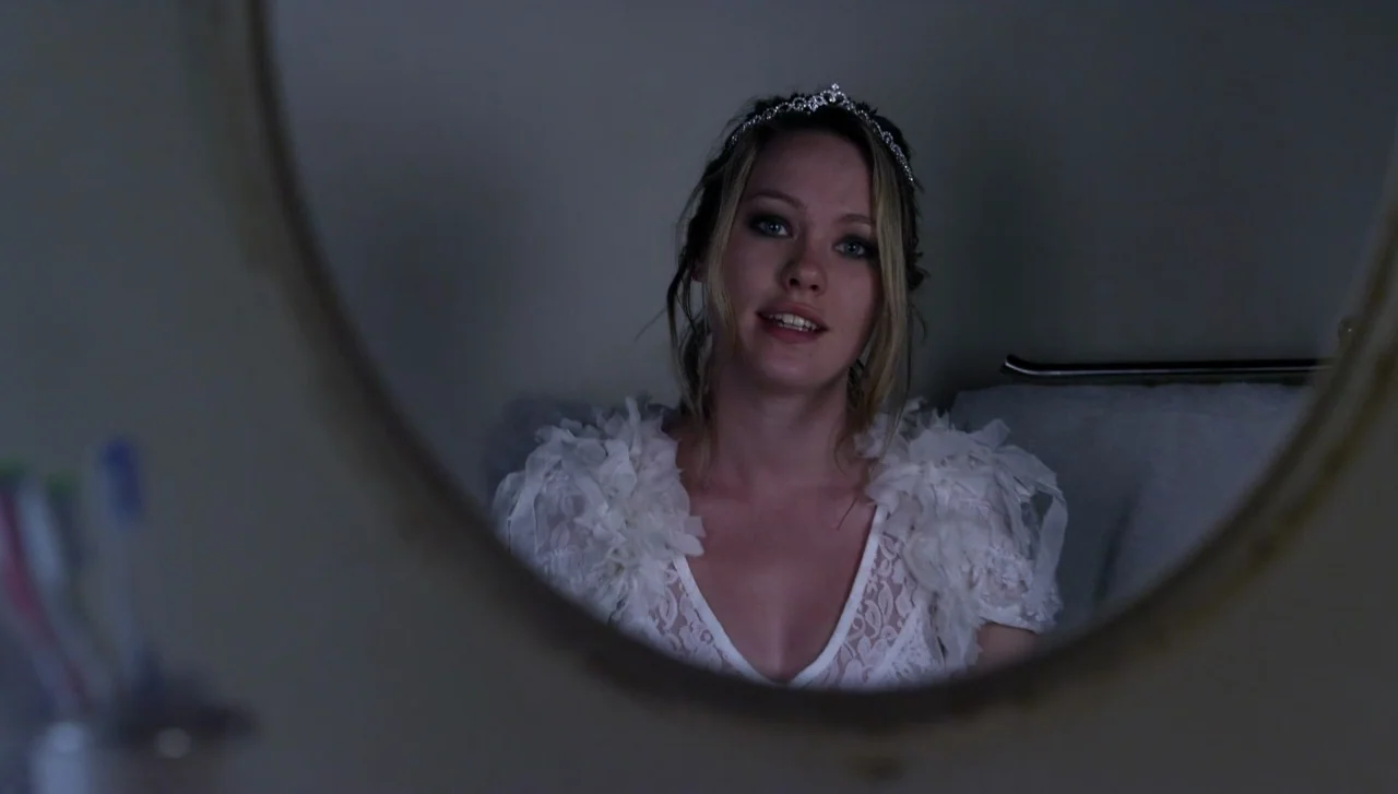 Hellions (2015) movie still: closeup — A woman in a white lace dress is reflected in a circular mirror. She looks at her reflection while standing…