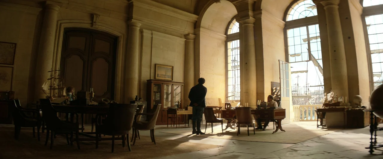 The Count of Monte-Cristo (2024) movie still: wide — A spacious, stone-walled room features high arched windows overlooking a harbor with ships. One…