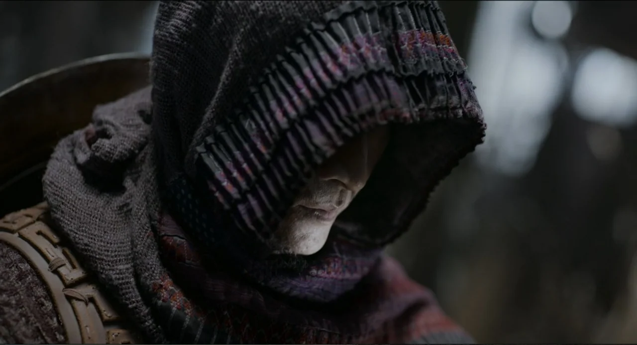 Legends of the Condor Heroes: The Gallants (2025) movie still: closeup — A dimly lit interior space features a figure draped in heavy, textured dark…