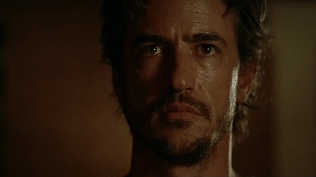 Undertow (2004) movie still: closeup — A man's face is shown against a dark, undifferentiated background. He looks forward with an steady, neutral…