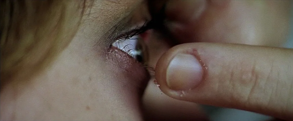 Anguish (1987) movie still: closeup — A close-up view shows a finger touching the lower eyelid of a person. The skin and eye are illuminated by…