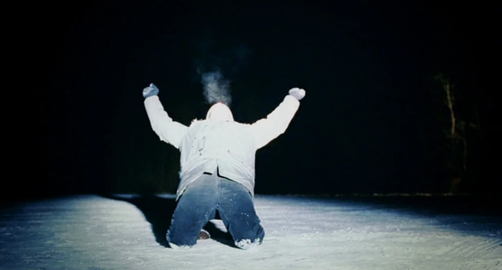Eternal Sunshine of the Spotless Mind (2004) movie still: fullbody — A person kneels on a snow-covered surface under dark night skies. The subject…