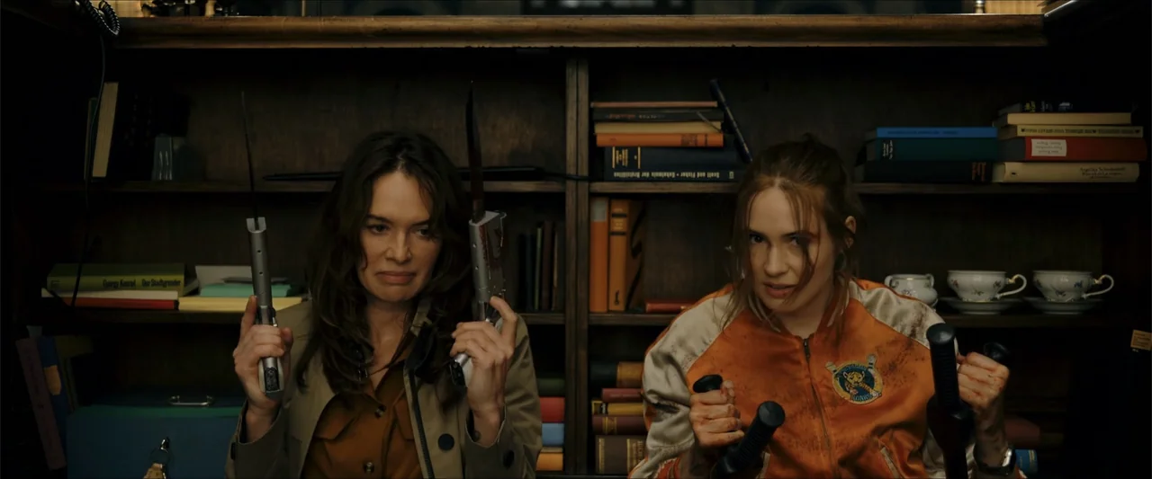 Gunpowder Milkshake (2021) movie still: medium — A dark library with floor-to-ceiling wooden bookshelves filled with various hardbound books. Two…
